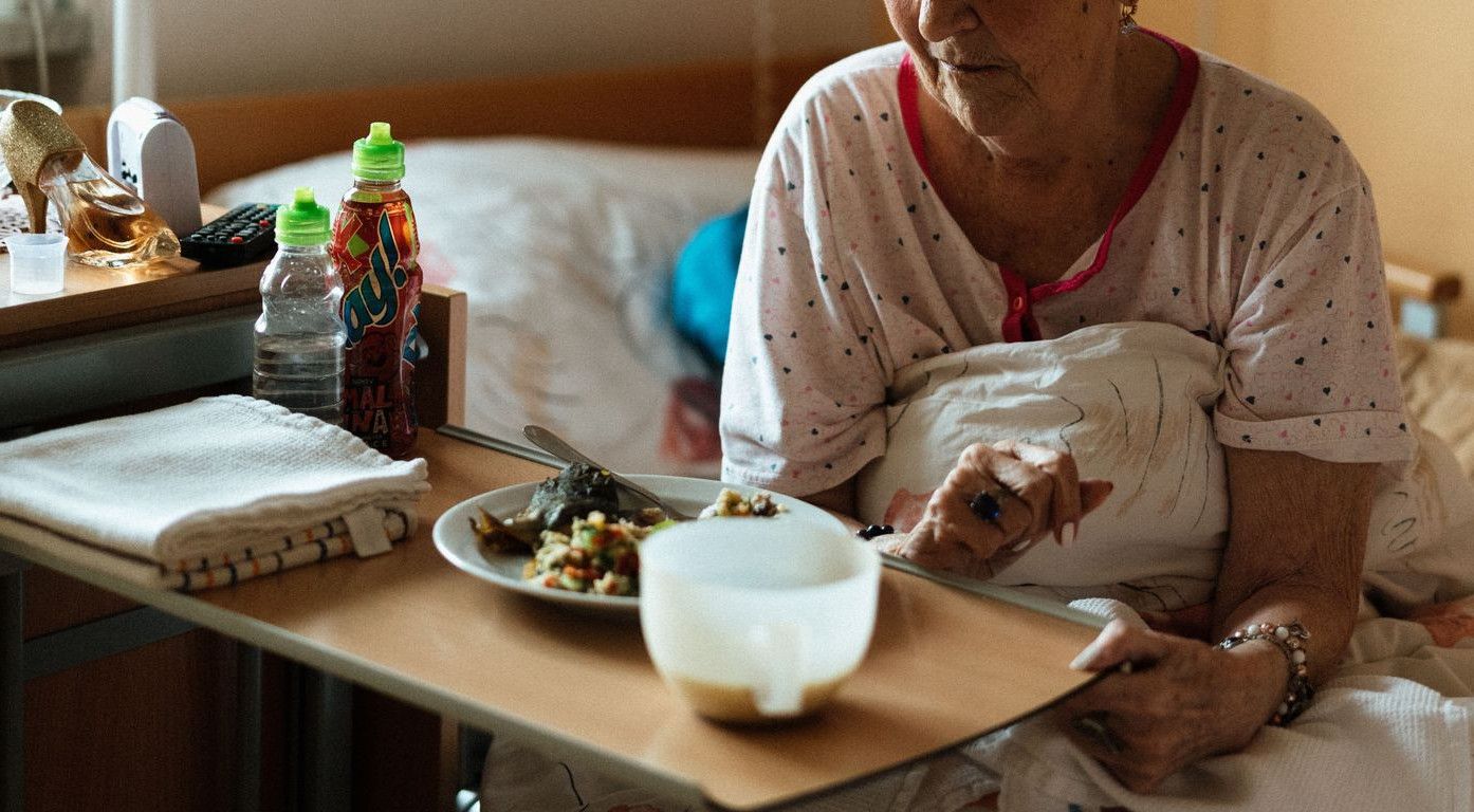 Elderly woman enjoying a meal in a cozy retirement home setting.